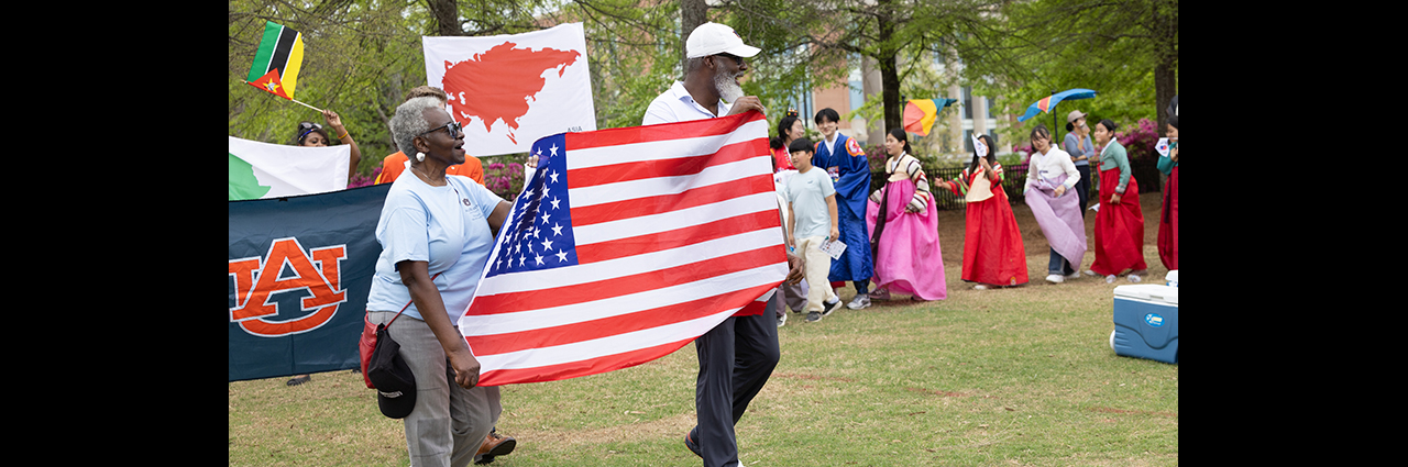 Man and woman carry American flag followed by a parade of others with flags.